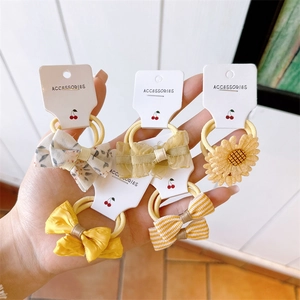 Detailed close-up of five yellow children's bow and flower hair ties on a display card