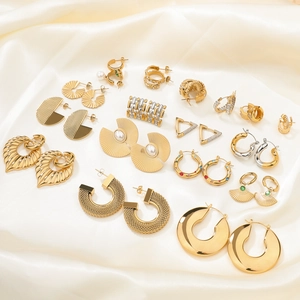 Flat lay of gold statement earrings with leaf pendants and zircon on beige silk