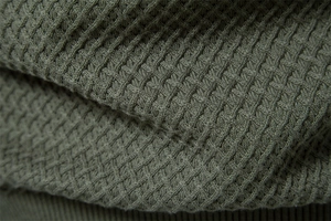 Detailed macro view of olive green waffle knit texture on cotton blend sweater fabric