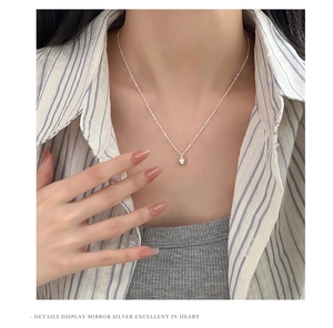 Mirror polished heart-shaped silver pendant necklace worn by a model on a minimal background