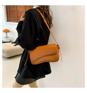 Detail view of brown shoulder bag with wavy flap design on female model in warm lighting