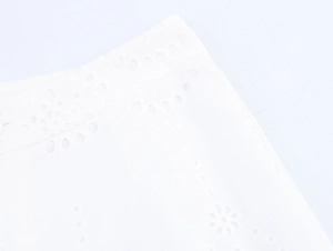 Detail shot of white high-waisted wide leg pants with intricate floral eyelet embroidery