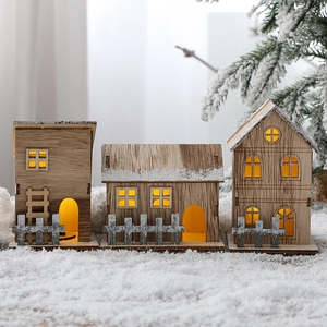 Three illuminated wooden Christmas houses on snow with pine branch decorations