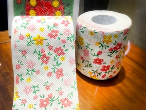 Detail view of colorful floral printed toilet paper rolls on a polished wood surface
