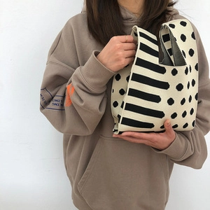 Detail of beige and black knit tote bag with polka dots and stripes held by a model