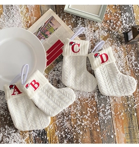 Detail of four white knitted Christmas stockings with embroidered letters A, B, C, D on wood