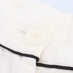 Detailed close-up of white linen fabric with a four-hole button and black piping trim