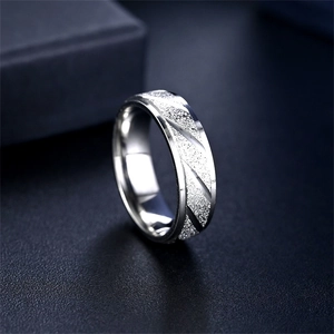 Dettaglio di un anello in acciaio al titanio argento con texture opaca e solchi diagonali.