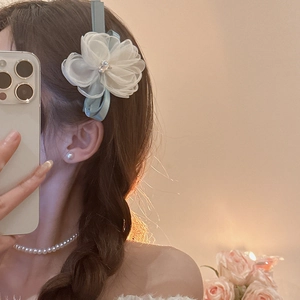 Detail of white organza flower hair clip with rhinestones and blue ribbon base
