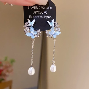 Detail of 925 silver butterfly earrings with dangling teardrop pearls on black packaging