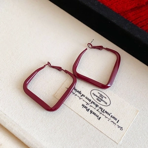 Détail des boucles d'oreilles créoles carrées bordeaux brillant sur une toile beige