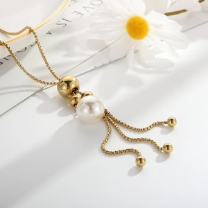Primo piano della collana dorata con pendente in perla bianca e nappa su fondo di margherite