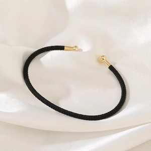 Detail shot of a black woven rope cuff bracelet with polished gold metal end caps