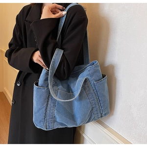 Blue denim tote bag shoulder carry view with side pocket on a black coat outfit