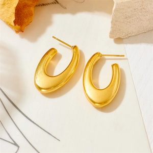 Detail shot of golden U-shaped geometric earrings on a minimalist textured surface