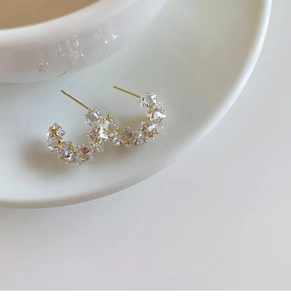 Close-up of gold C-shaped earrings with clear zircons on white ceramic tray