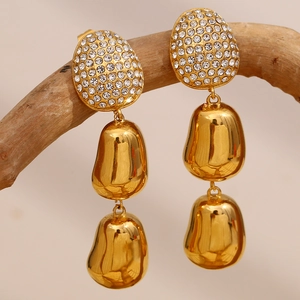 Detailed shot of long gold earrings with rhinestone studs hanging on a wooden branch