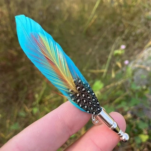 Peacock feather brooch with silver base for men's suit held over a grassy background