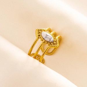 Macro shot of gold-plated twisted ring with marquise white marble stone on beige fabric