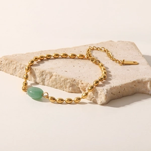 Detailed shot of golden beaded bracelet with green oval stone on a stone pedestal
