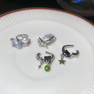 Macro shot of silver ear cuffs set with zircon, pearls, and black cat star charms on white tray