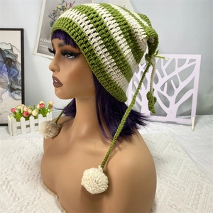 Detail of green striped knit hat with cute cat ears, braided cords and fluffy pom-poms