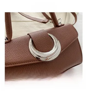 Détails de la boucle argentée en demi-lune sur le sac en cuir marron à grain litchi