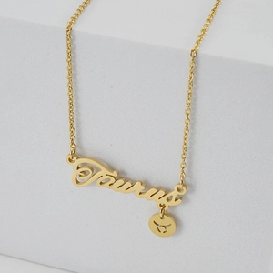 Collar Tauro dorado con colgante de letra sobre un soporte geométrico blanco