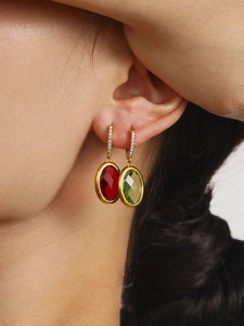 Close-up of gold hoop earrings with faceted red and green gemstones on a model
