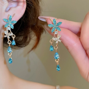 Detail of flower and teardrop earrings with blue and clear crystals on a golden frame