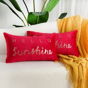 Detail of two red velvet pillow covers with gold Sunshine embroidery on a white sofa