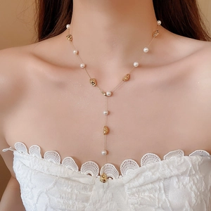 Dettaglio di una collana a Y placcata in oro con perle irregolari su una modella donna