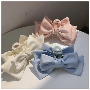 Three large matte satin bow hair clips in pink, beige, and light blue on a white table