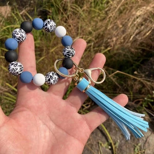 Handheld view of a blue and leopard print beaded bracelet keychain with PU tassel detail