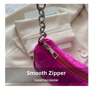 Detail of smooth metal zipper and silver chain on a pink quilted crescent bag