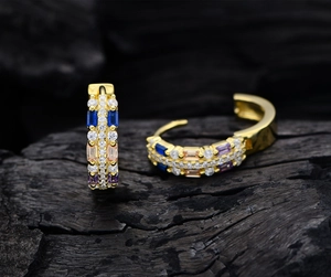 Detailed close-up of 18K gold hoop earrings with multi-colored cubic zirconia on dark wood