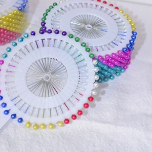 Colorful pearl head sewing pins set organized in round wheels on white fabric background