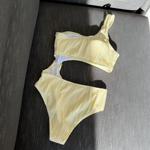 Detail of light yellow textured one-shoulder swimsuit with waist cutout on grey fabric