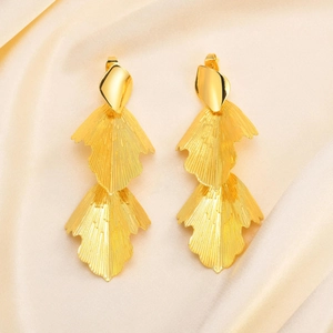 Golden double-layer leaf dangle earrings with textured finish on silk background