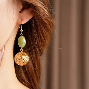 Model wearing gold hollow ball earrings with green jade stone and vintage fishhook