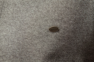 Macro view of grey-brown knit fabric texture with a bronze-toned metal logo badge
