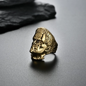 Macro detail of a 18K gold-plated Frankenstein head ring on a textured black surface
