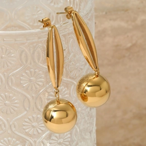 Detail of gold hollow ball earrings hanging on a decorative glass texture