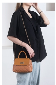 Close-up of caramel brown quilted handbag with gold chain strap worn on a black blazer