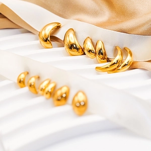 Polished gold stud earrings in drop and crescent shapes on champagne silk background