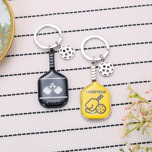 Detail of yellow and black metal pickleball racket keychains on a textured surface