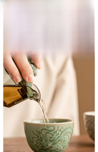 Detail of tea pouring into a celadon ceramic cup featuring an embossed dragon pattern