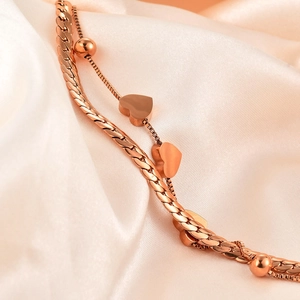 Macro shot of rose gold layered heart bracelet with snake chain on white silk