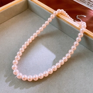 Close-up of pink pearl necklace with silver clasp on a grey velvet jewelry tray