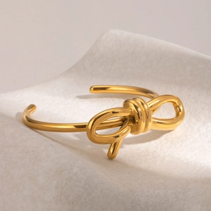 Detailed close-up of polished gold bow-shaped open bangle on white stone stand
